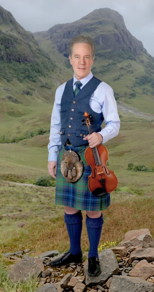 Jamie Laval holding his fiddle against a mountain landscape in the Scottish Highlands