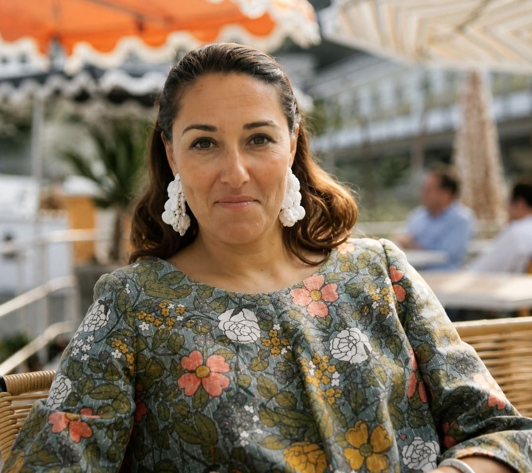 Elettra in a floral dress and statement earrings, photographed beneath a striped awning.
